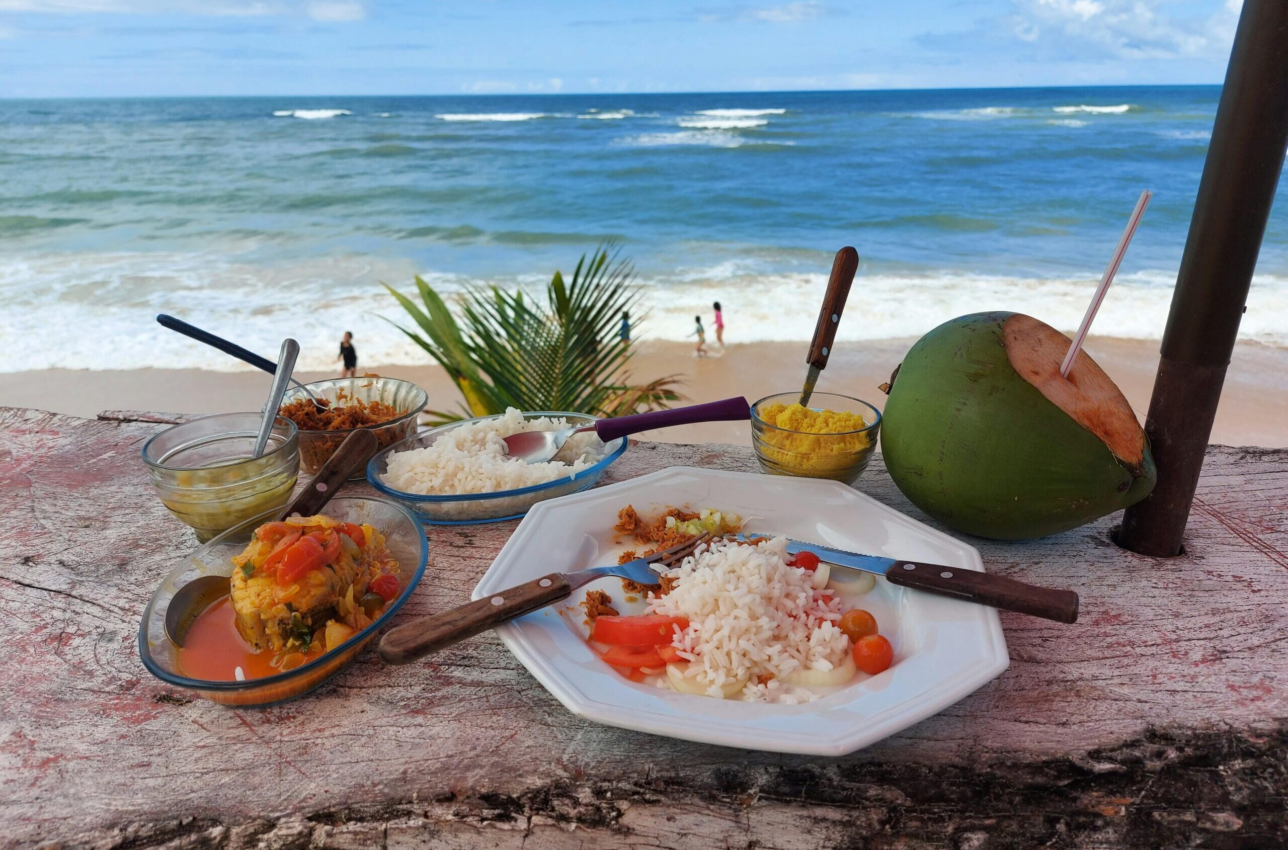 Tropical meal with rice and curry, served by the beach with coconut water and ocean view.